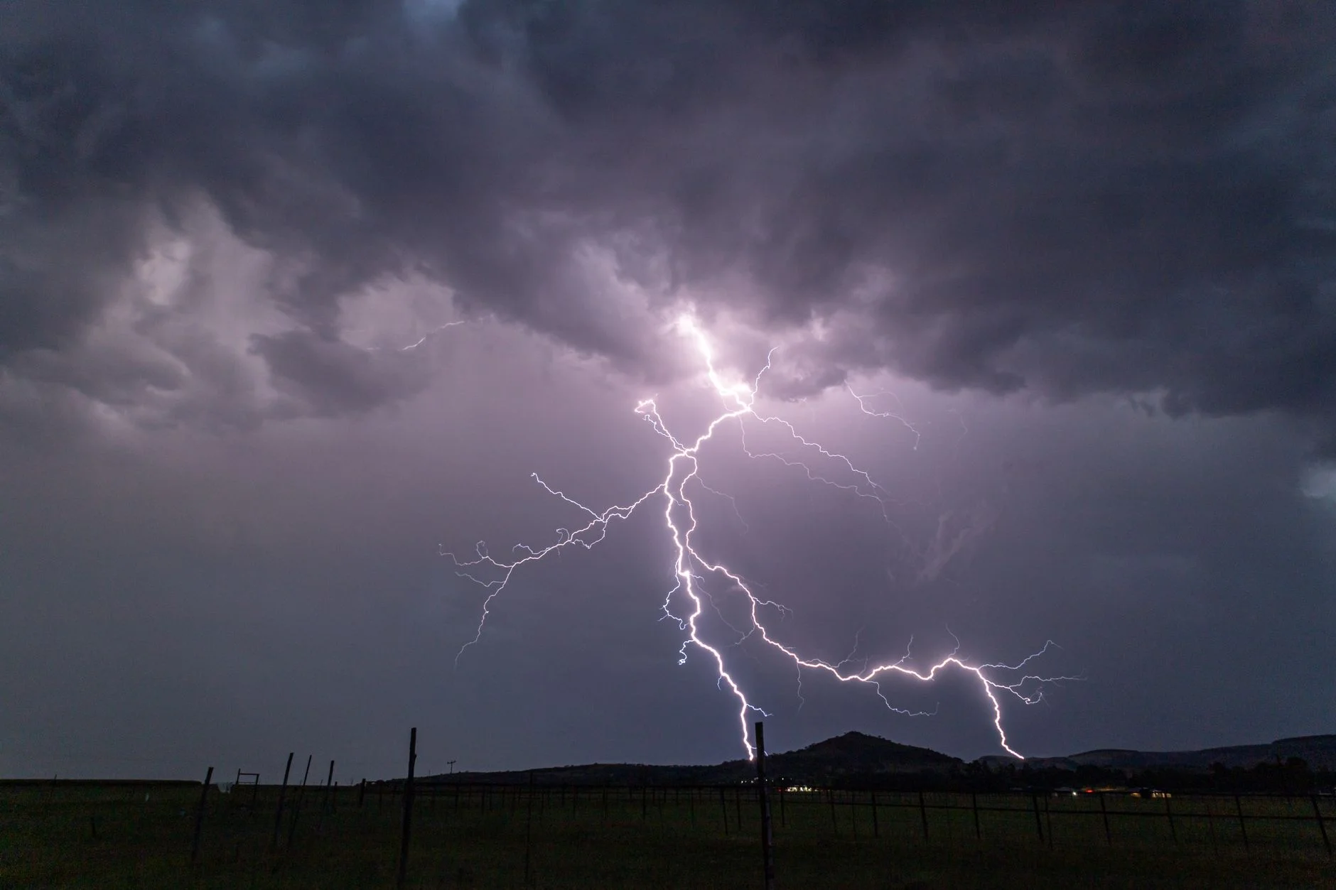 A purple-lit storm cloud with a cloud-to-ground lightning strike over flat land