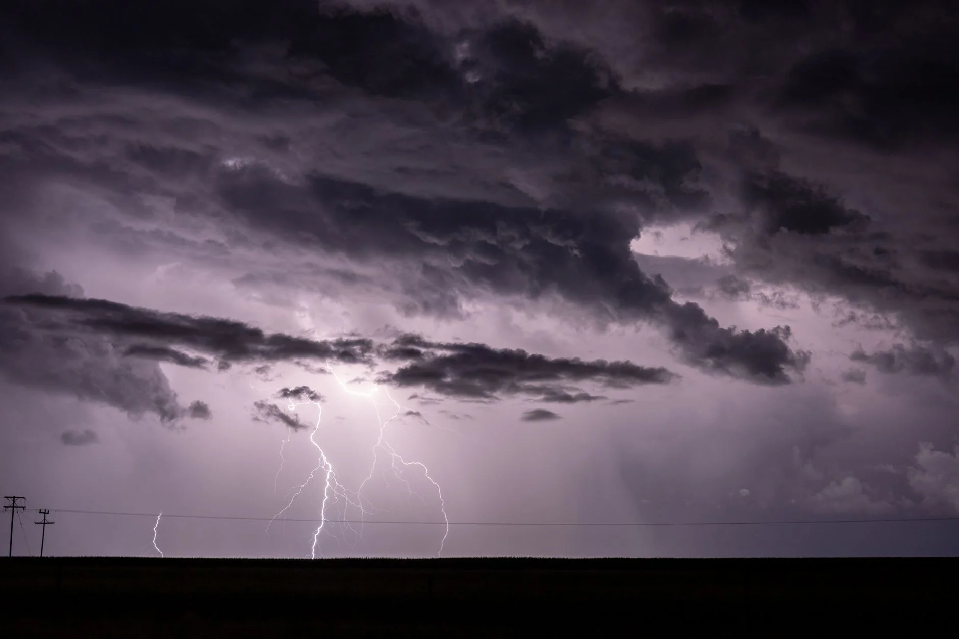 Lightning bolts under dark storm clouds over flat farmland