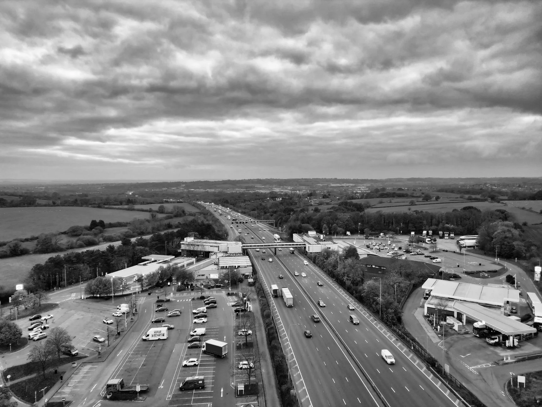Black-and-white aerial view of a busy UK motorway with a service area and car parks on both sides