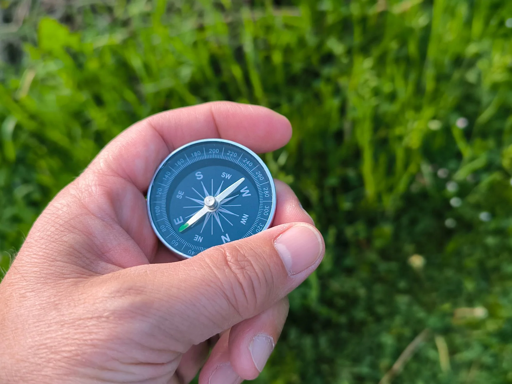 A hand holding a small blue magnetic compass against green grass