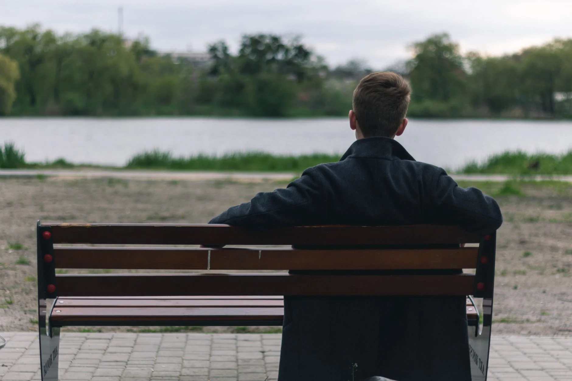 Man sitting alone on a park bench facing a lake