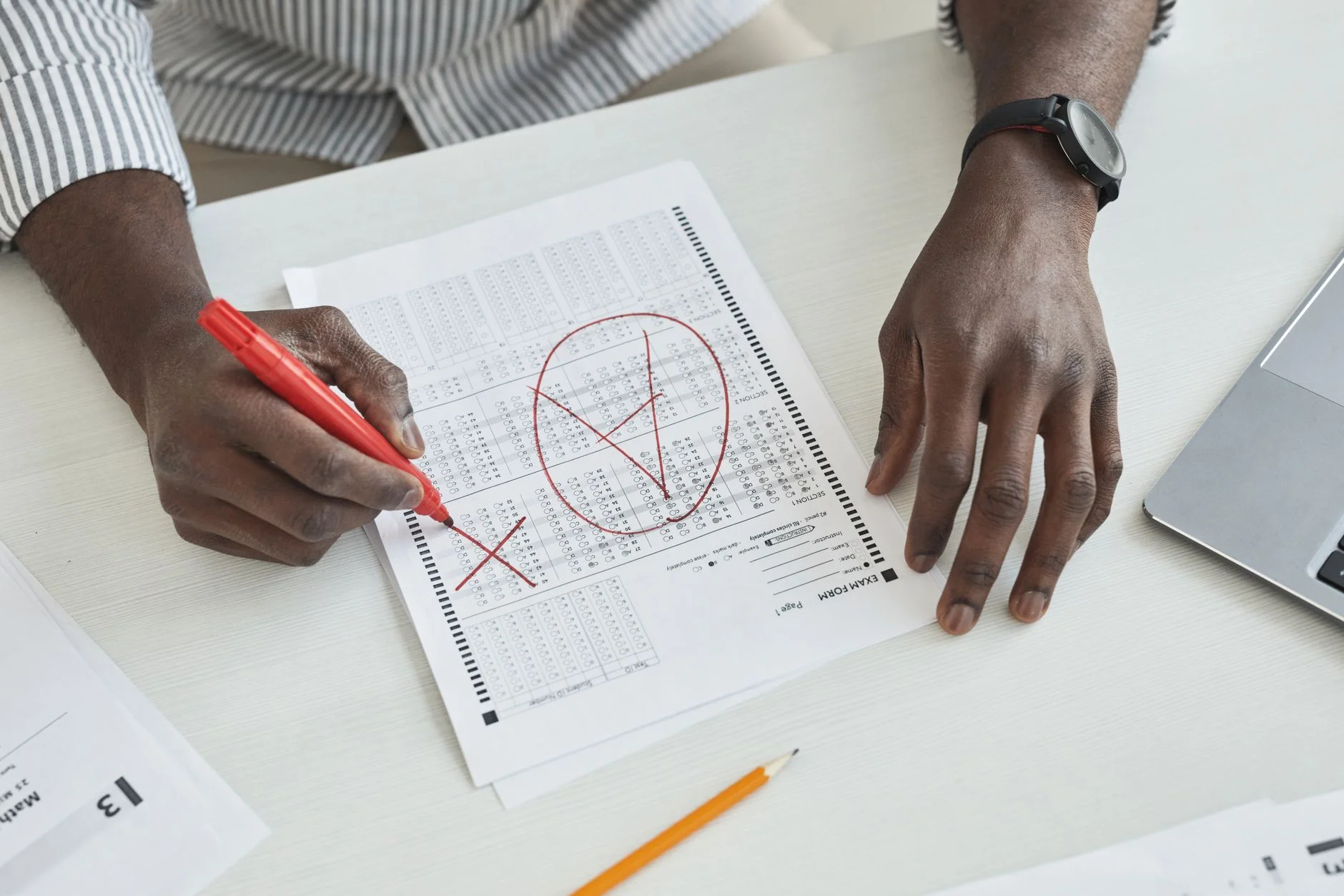 Hands marking a paper with a red pen, with crosses and a circled answer