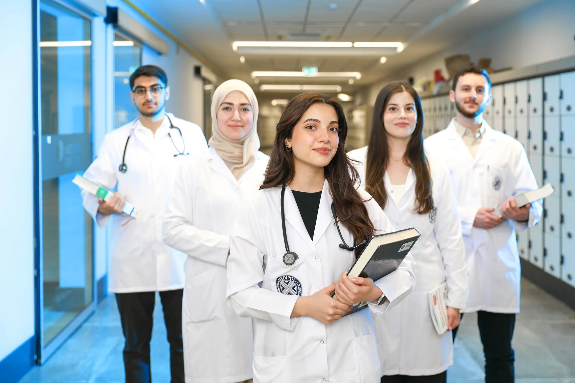 A group of medical students in white coats with stethoscopes standing in a university corridor