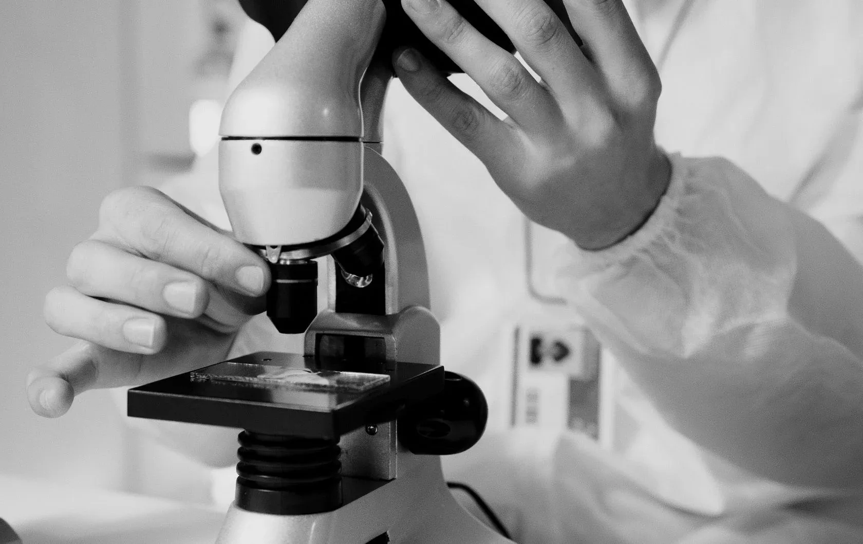 Black and white photo of a researcher in a lab coat adjusting a microscope