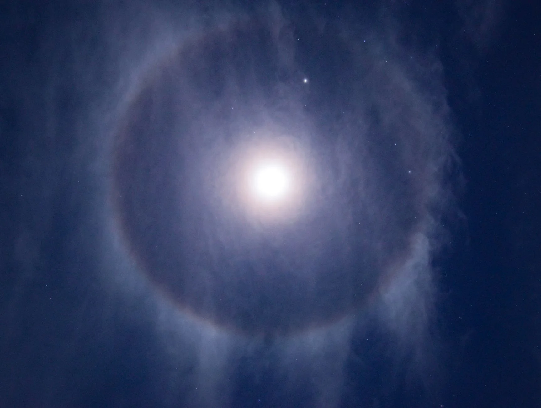 A moon halo ring around the bright Moon in a night sky with stars