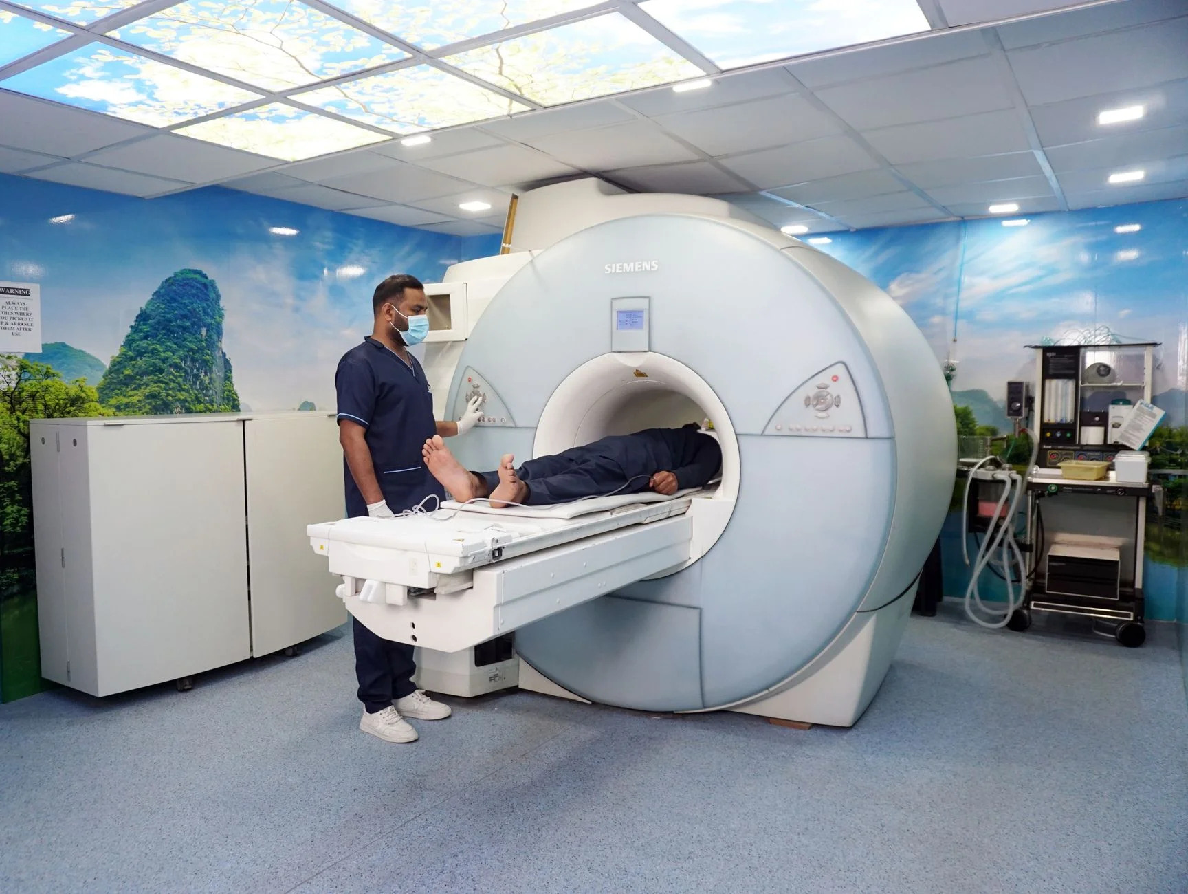 A radiographer standing beside a patient lying on the table as it moves into an MRI scanner