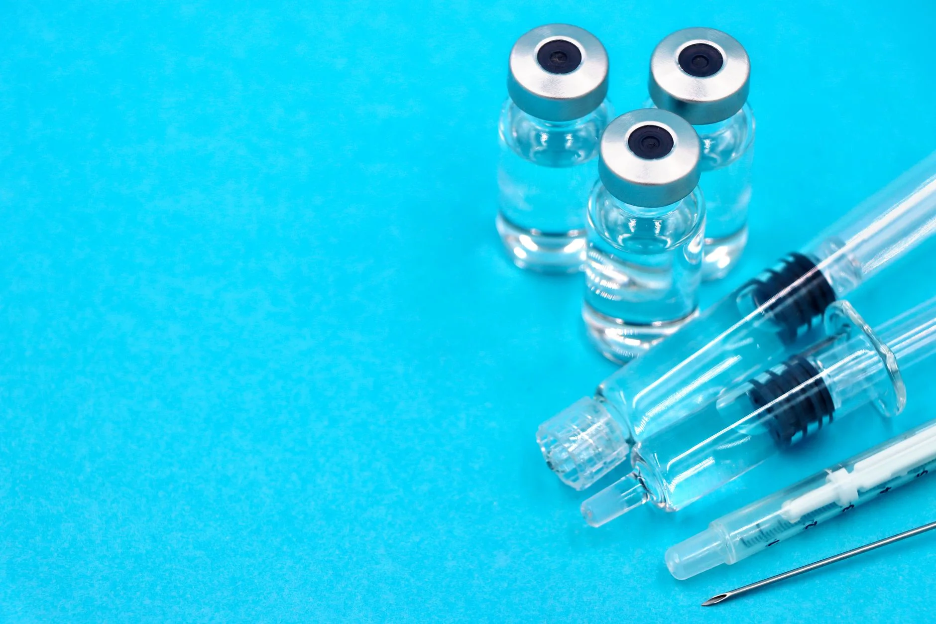 Three small glass vaccine vials and syringes on a bright blue background