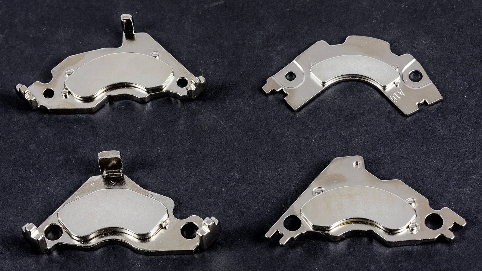 Four hard disk drive magnet assemblies: curved neodymium magnets fixed to shiny nickel-plated steel plates, on a dark background
