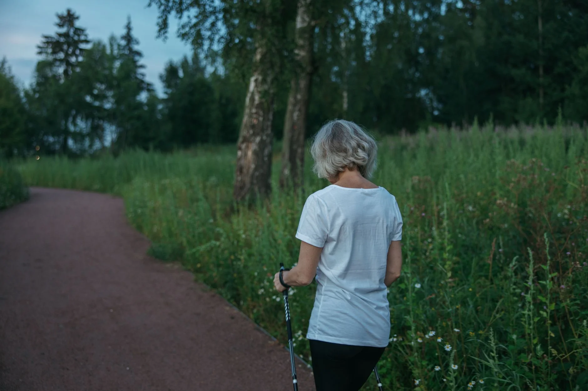 A woman with walking poles strolling along a path beside long grass in a park