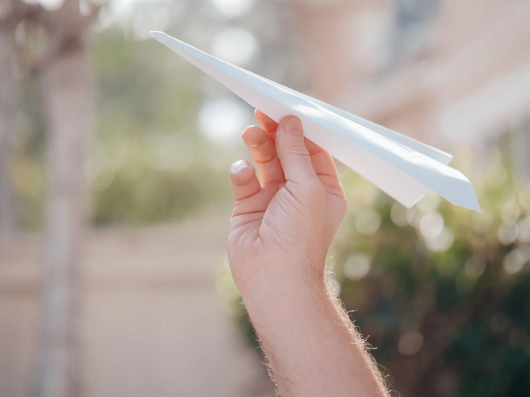 A hand holding a white paper aeroplane in sunlight