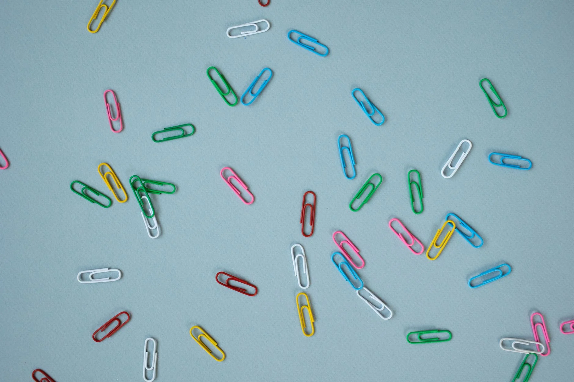 Colourful paper clips scattered on a pale blue surface