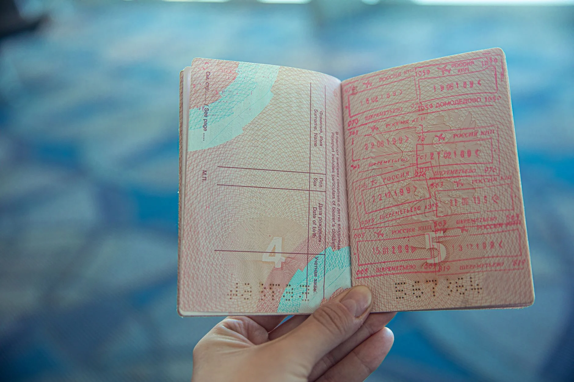 A hand holding an open passport full of red entry and exit stamps