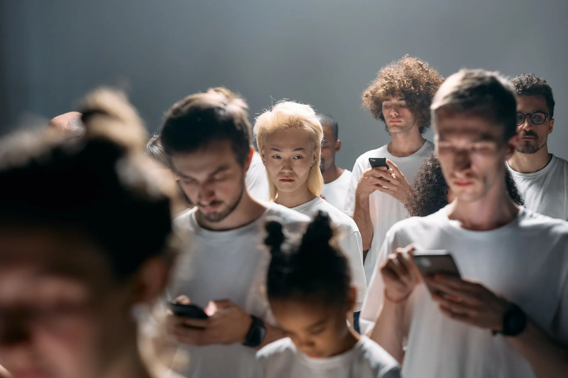 A group of young adults in white t-shirts all looking down at their smartphones
