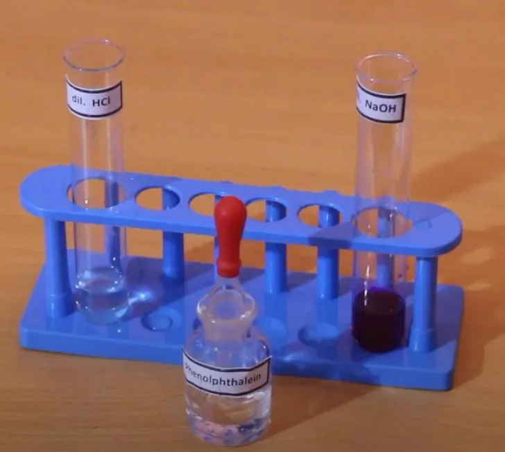 Phenolphthalein colourless in dilute hydrochloric acid and deep pink in dilute sodium hydroxide in test tubes on a blue rack