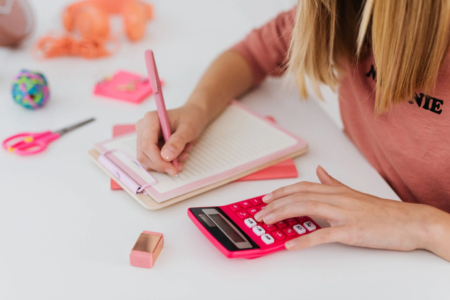 A student writing in a notebook while using a pink calculator