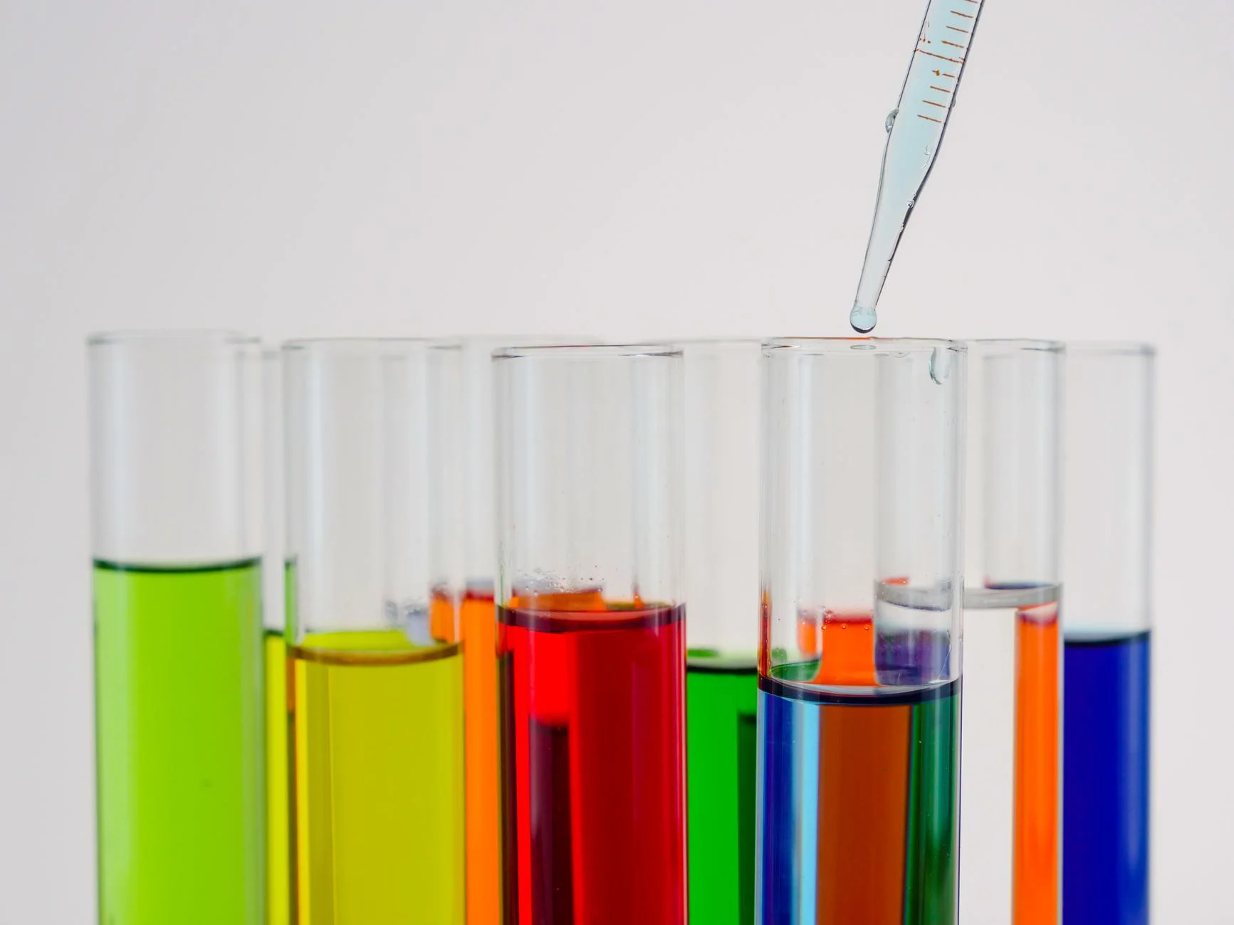 A dropping pipette above a row of test tubes filled with green, yellow, orange, red and blue liquids
