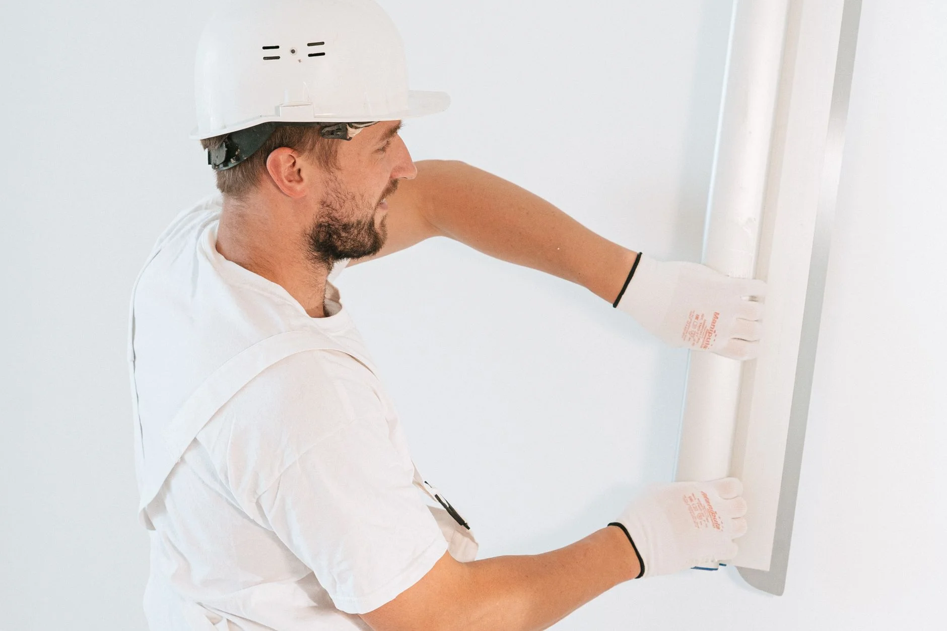 Worker in a hard hat and gloves holding a white board against a white wall