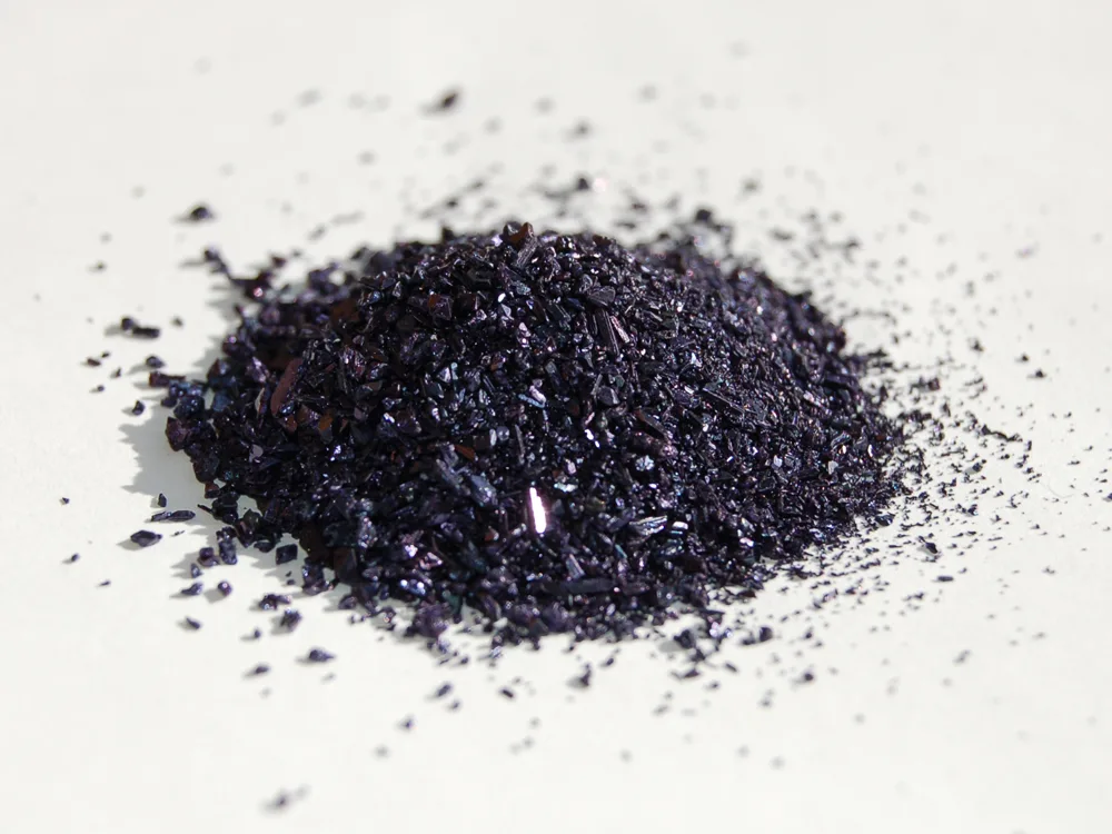 A small heap of dark purple, almost black potassium permanganate crystals on a white surface