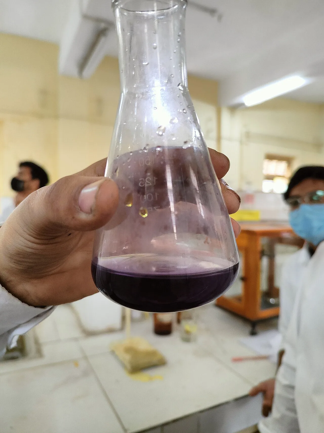 A student holding up a conical flask containing purple potassium permanganate solution in a school laboratory