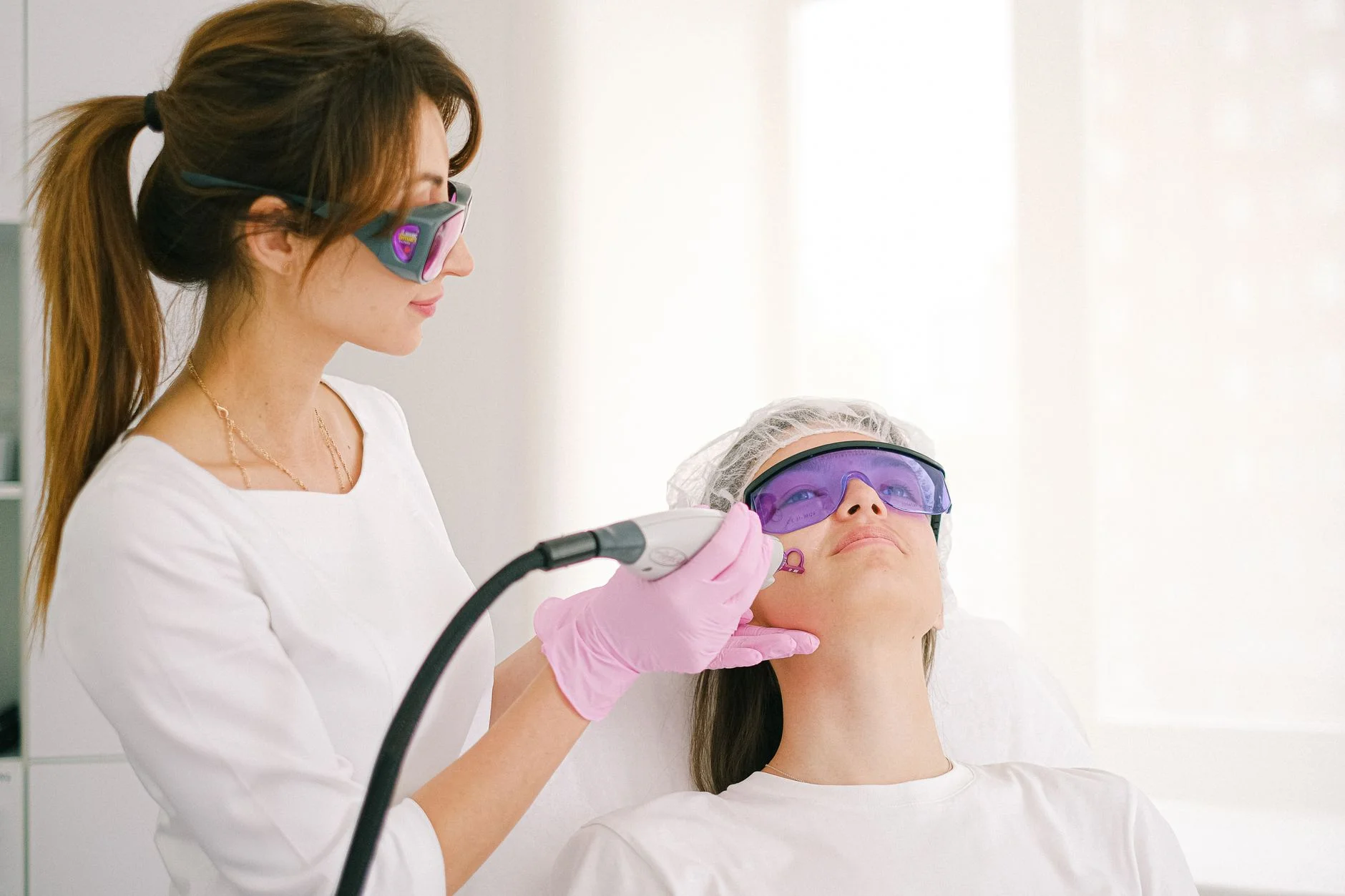 A practitioner and a client both wearing tinted protective eyewear during a laser treatment on the face