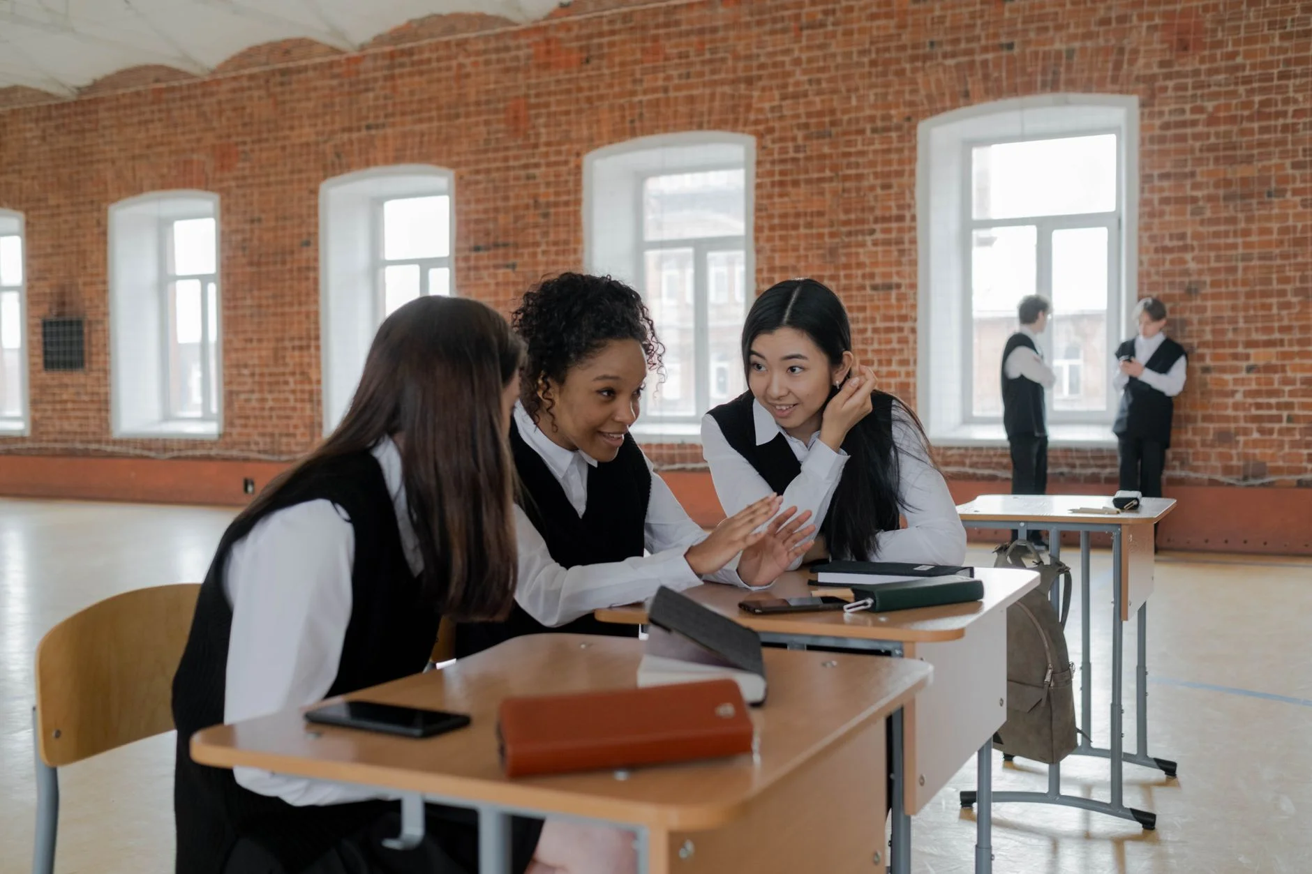 Three pupils in school uniform leaning in to talk and listen to each other at a classroom desk
