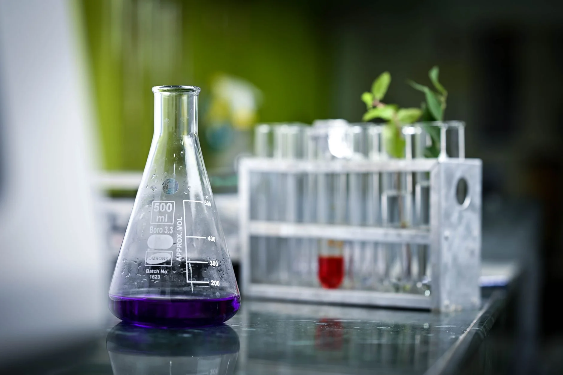 A conical flask holding a purple solution on a laboratory bench next to a rack of test tubes