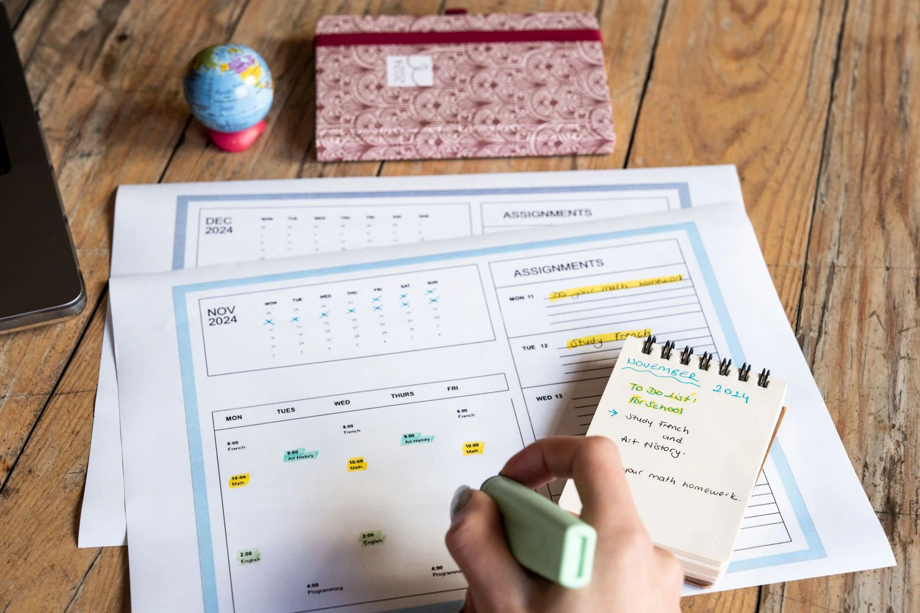 A person writing in a monthly planner with a highlighter pen, with a notepad of to-do items on top