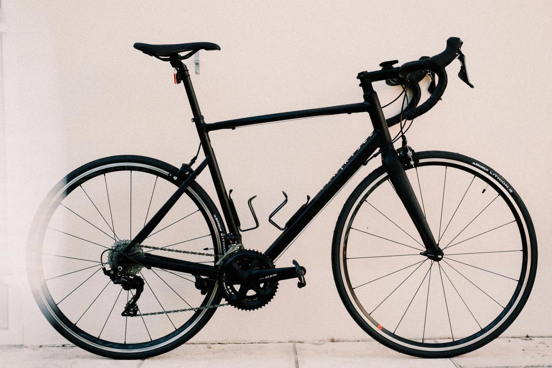 Black road bike with drop handlebars against a pale wall