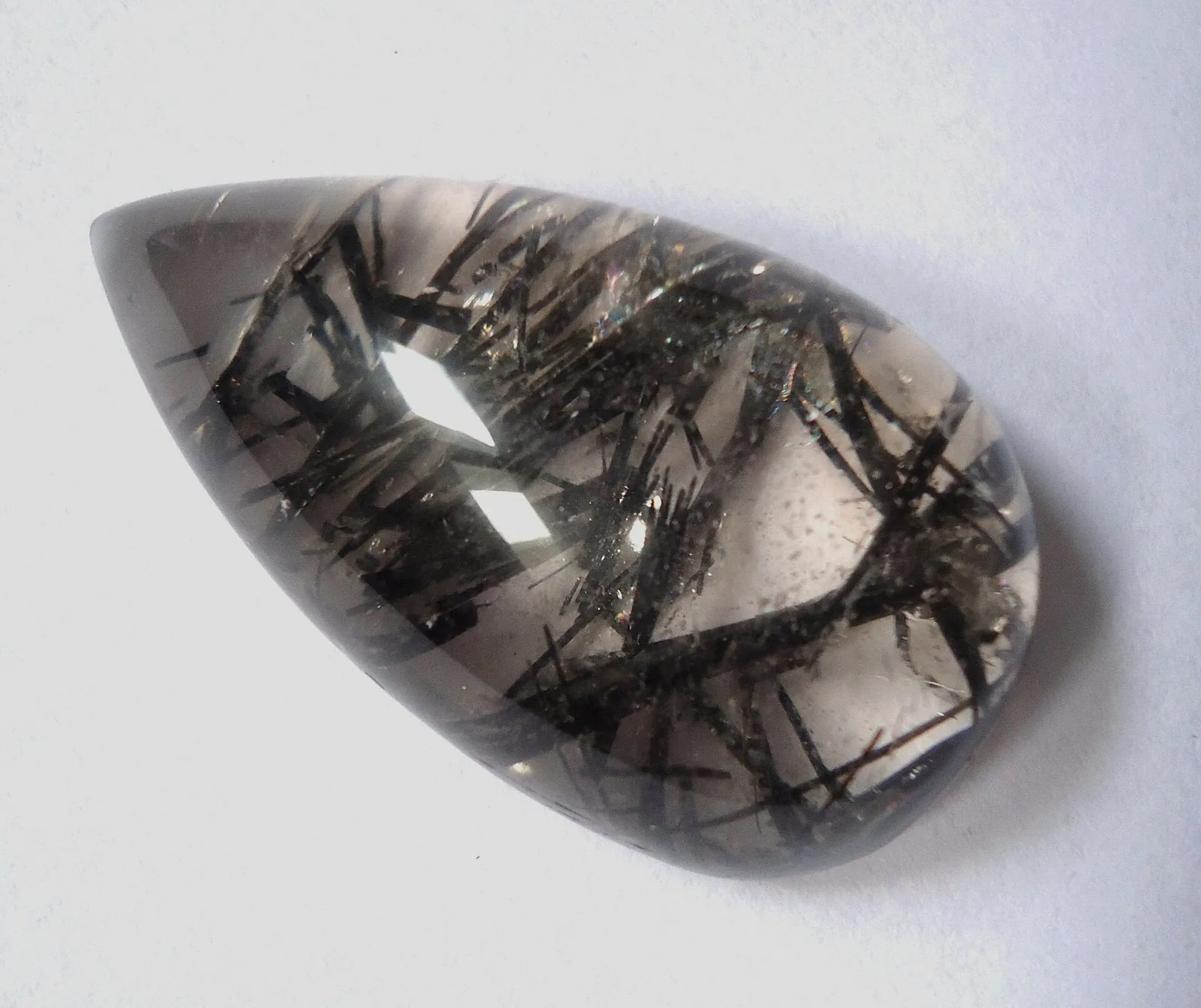 A polished smoky-grey quartz stone with dark needle-like rutile crystals inside