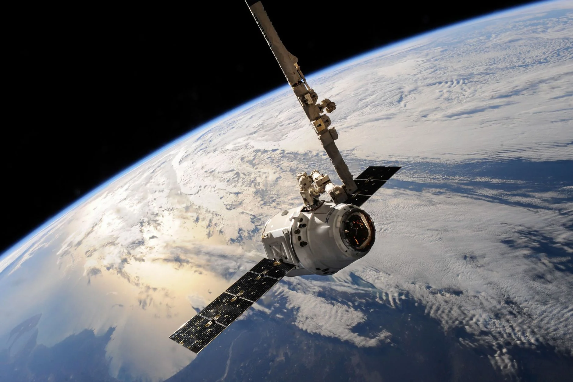 A spacecraft held by a robotic arm high above Earth’s clouds