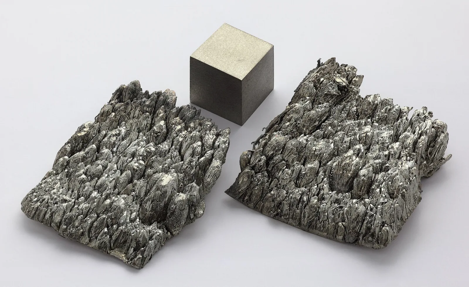 Sublimed dendritic scandium metal pieces beside a 1 cm cube of scandium