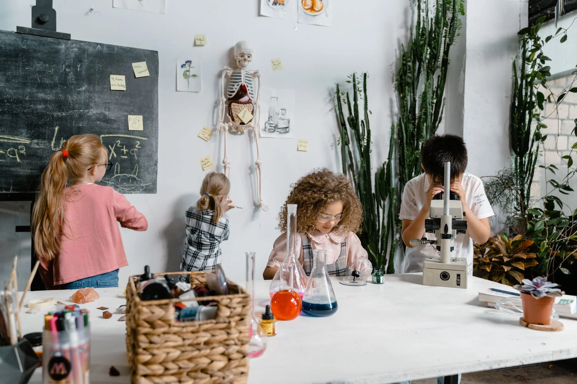 Children in a bright classroom working with flasks of coloured liquid and a microscope