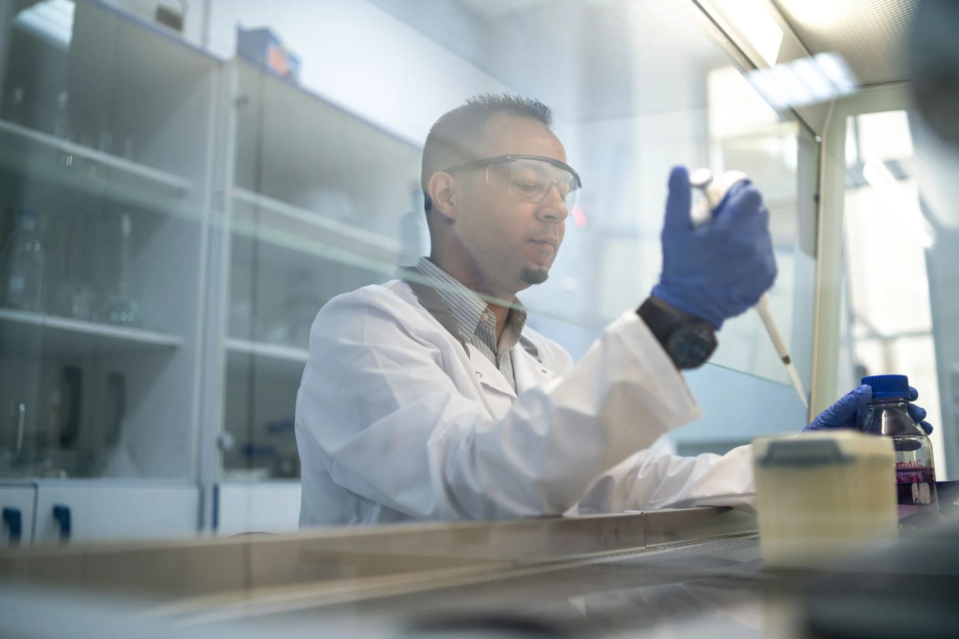 A scientist in safety glasses and a lab coat using a pipette in a laboratory