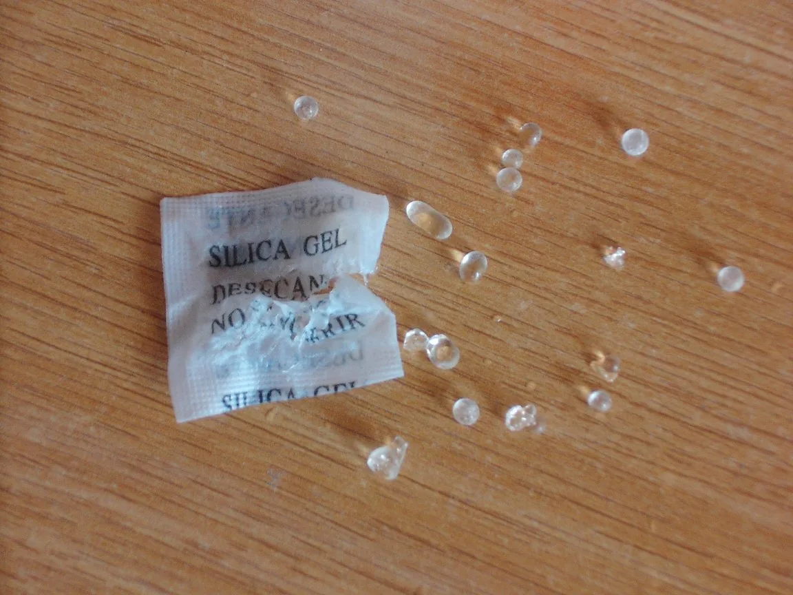 Clear silica gel beads spilling from a small desiccant packet