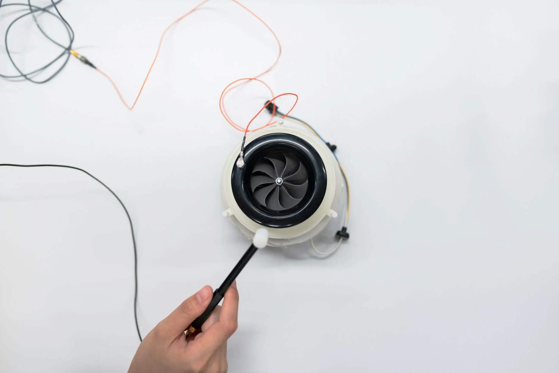 A small electric fan with a black rotor, connected by thin wires, being adjusted by a hand on a white desk