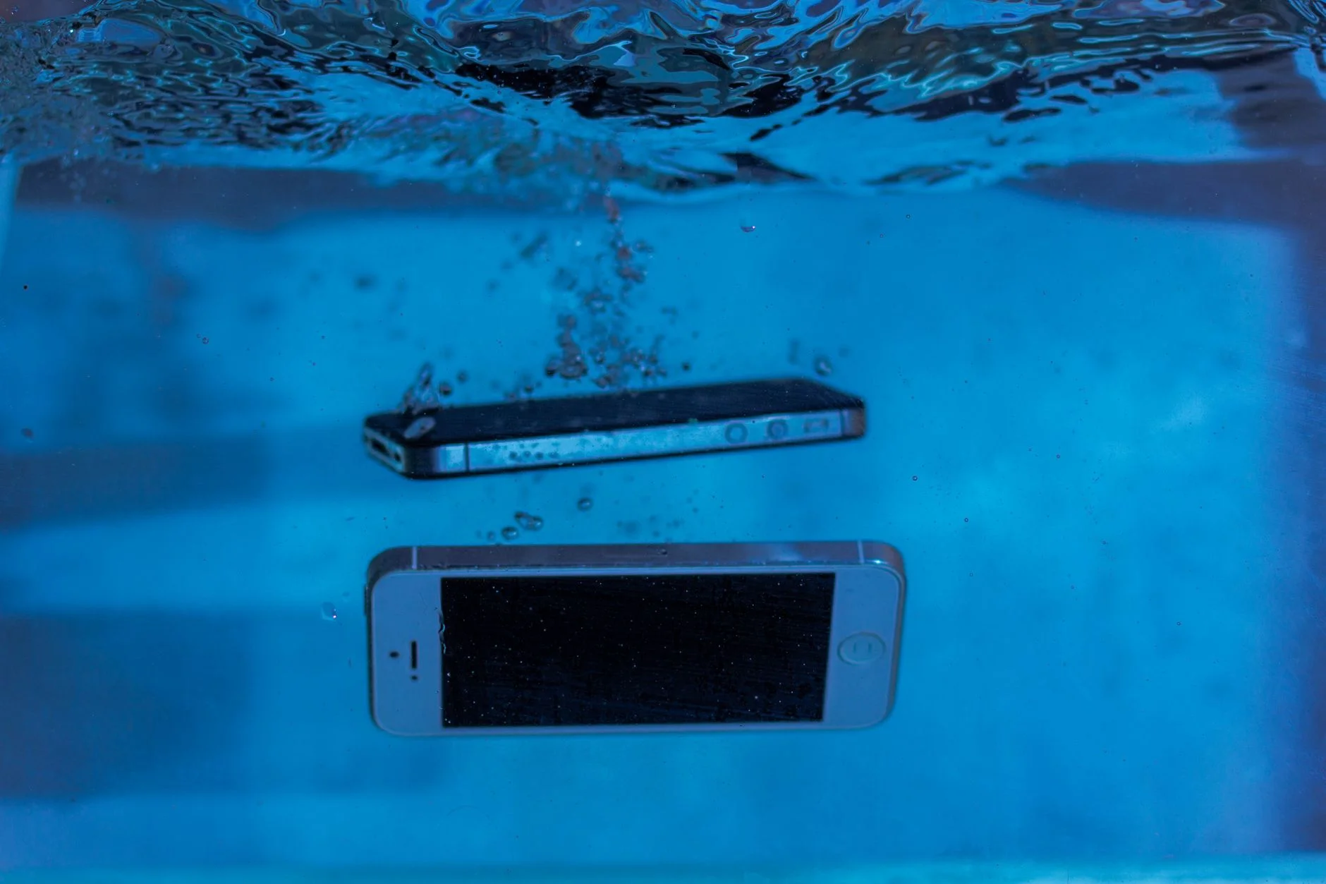 Two smartphones sinking in a tank of clear blue water