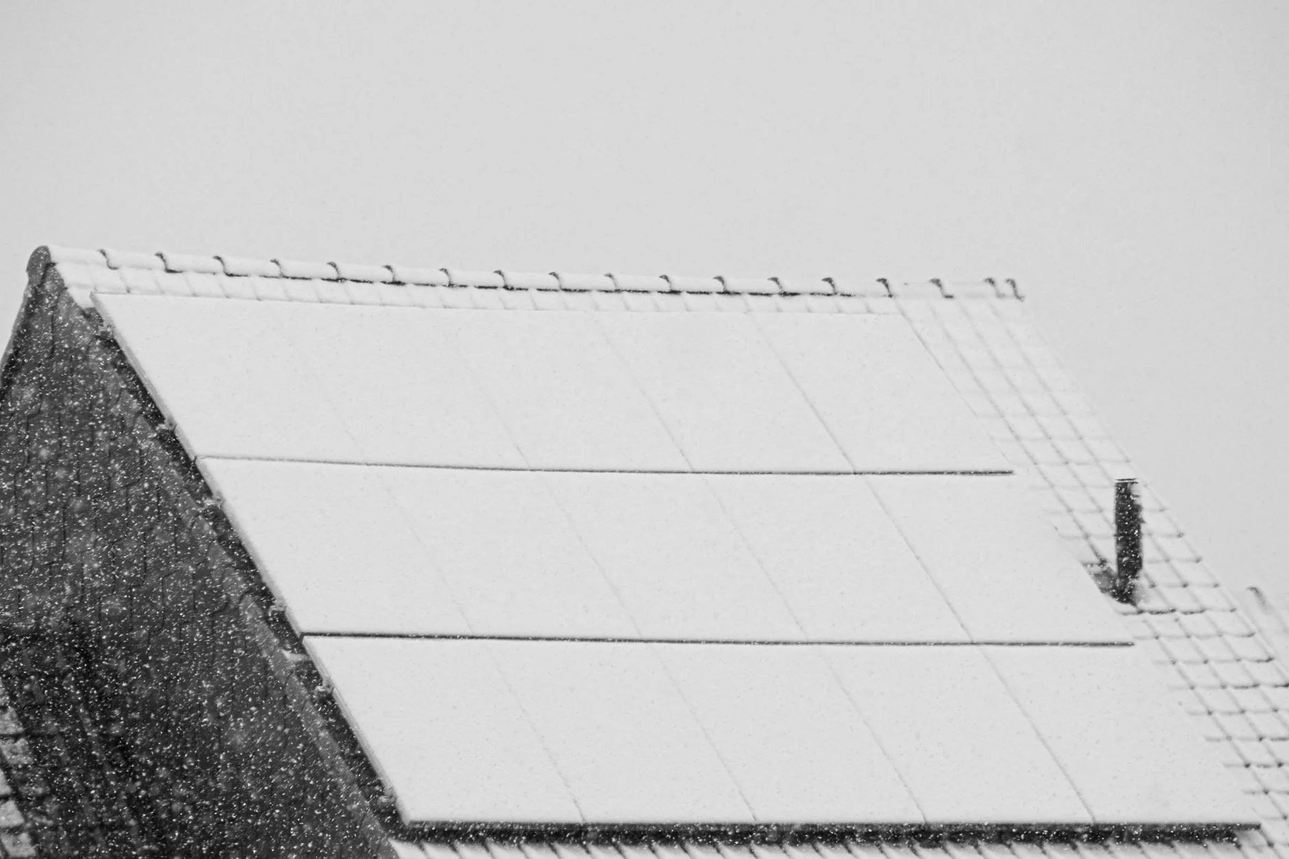 Solar panels on a pitched roof covered in snow during heavy snowfall