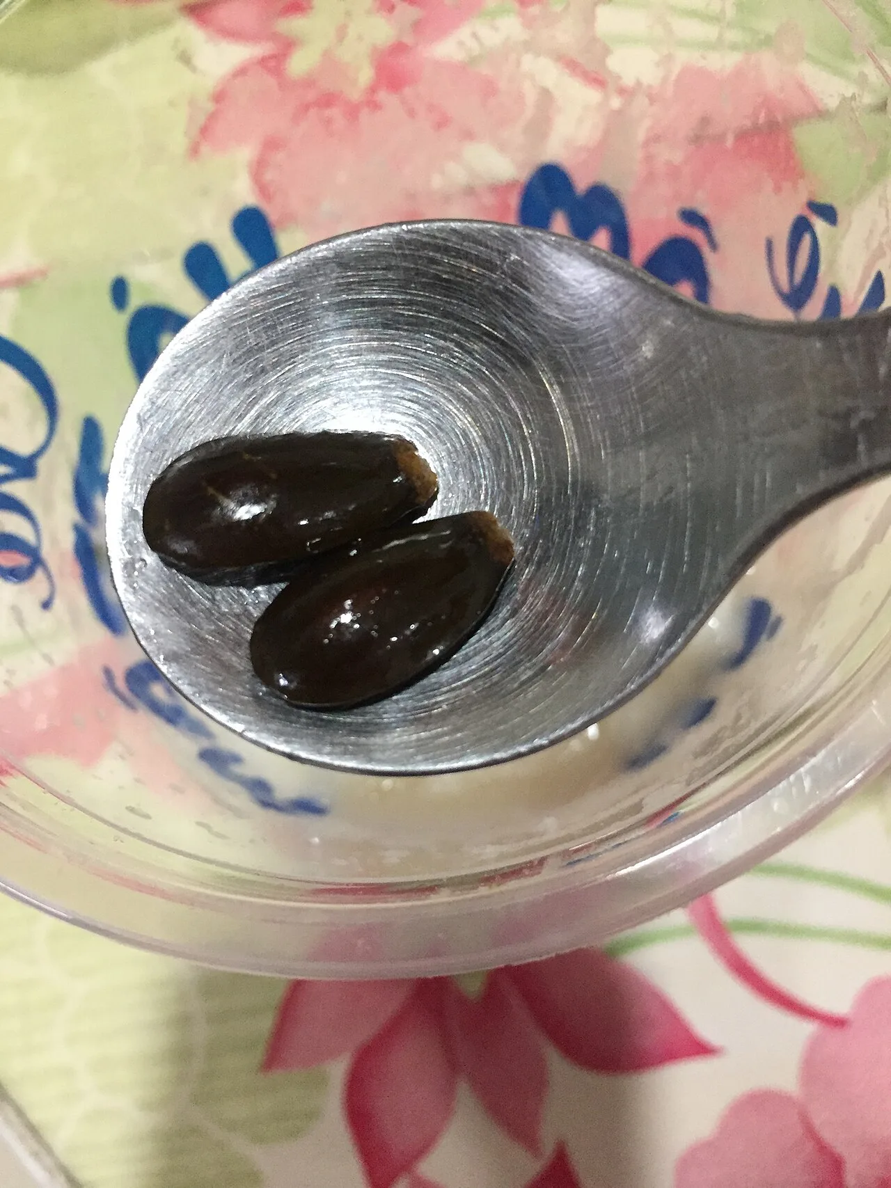 Two shiny black soursop seeds in a metal spoon