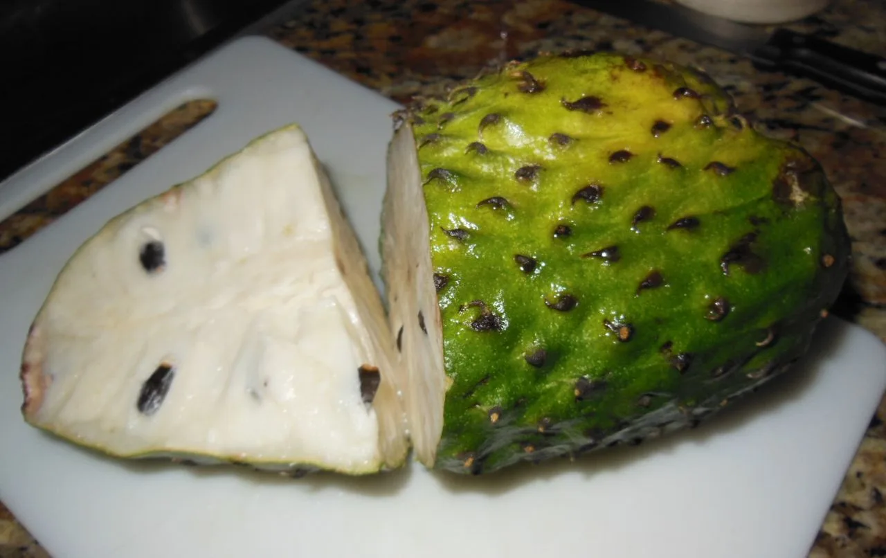 A soursop cut into a wedge on a white chopping board