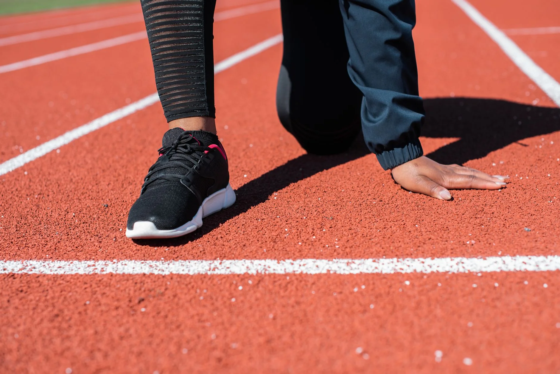 A runner crouching at the start line of a red running track with one hand on the ground
