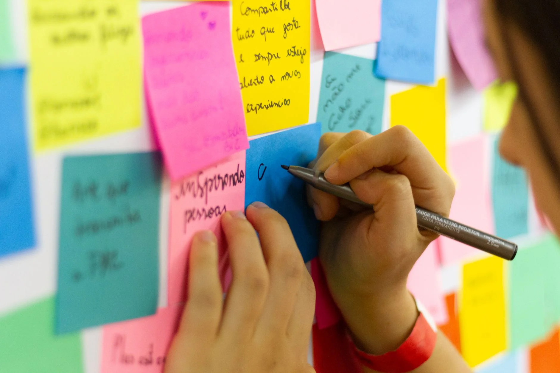 A hand writing on a colourful wall of sticky notes during a brainstorming session
