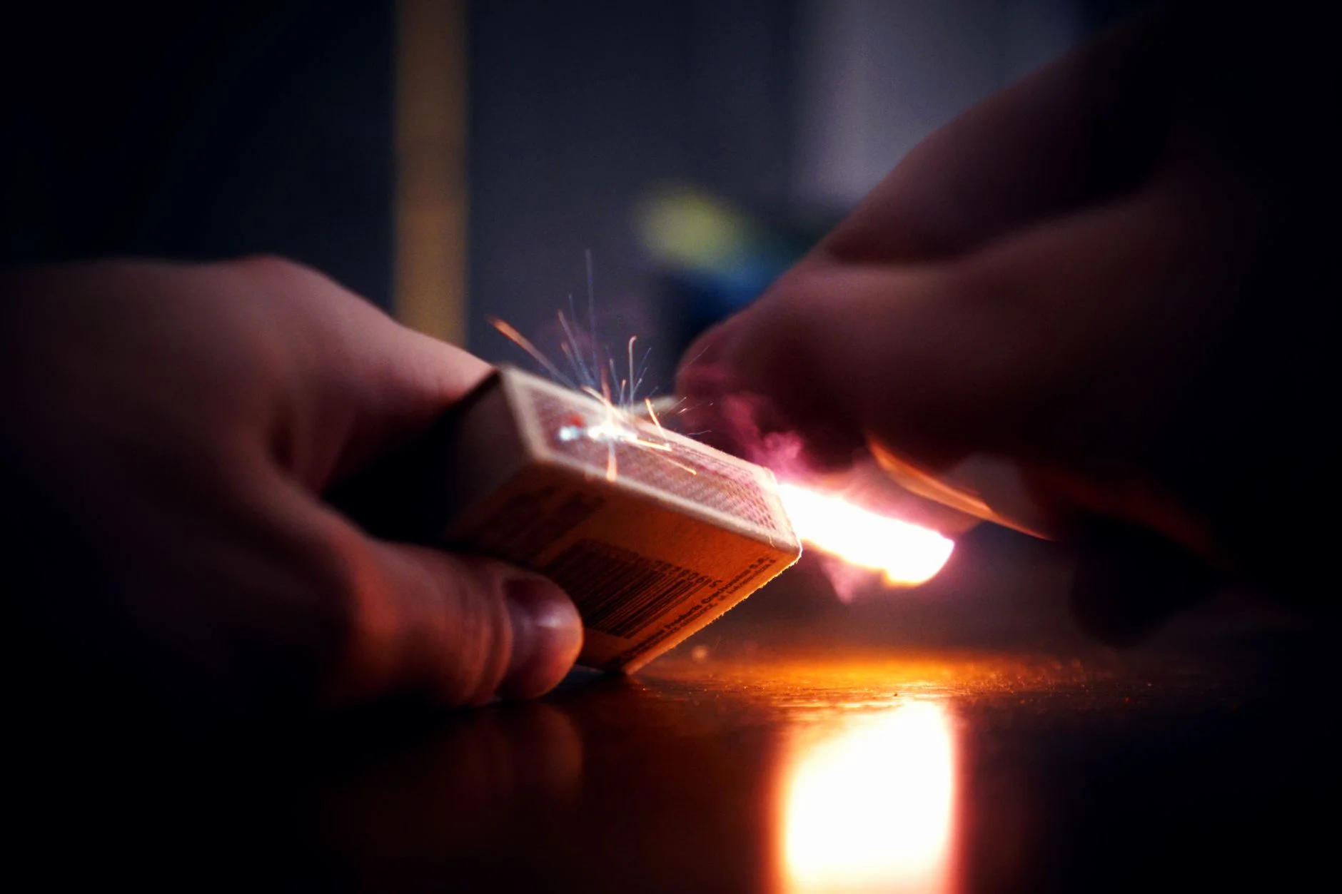 A hand striking a match against the side of a matchbox, with sparks and a bright flame