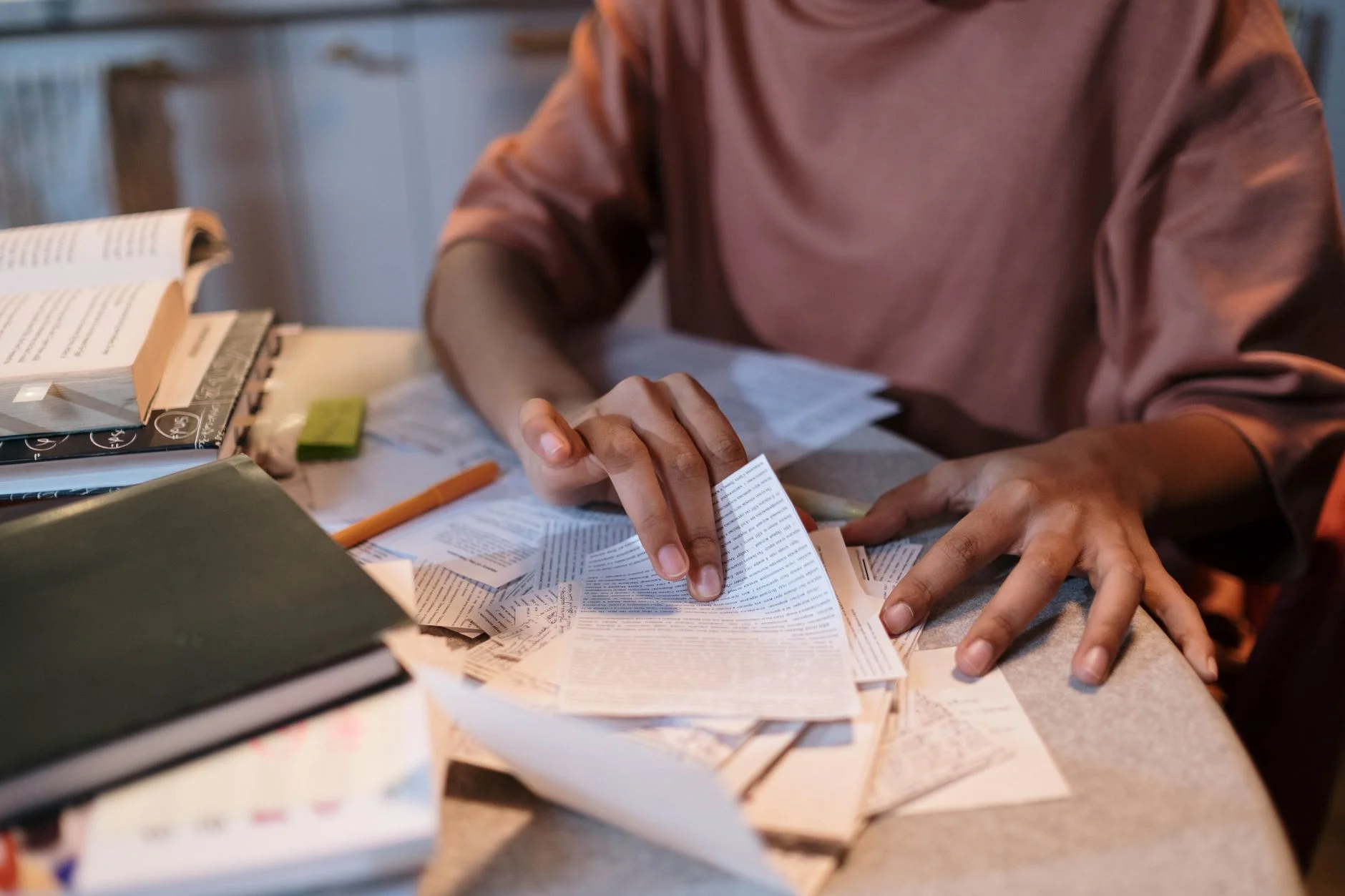 A student sitting at a table sorting through textbooks, notes and loose pages while revising