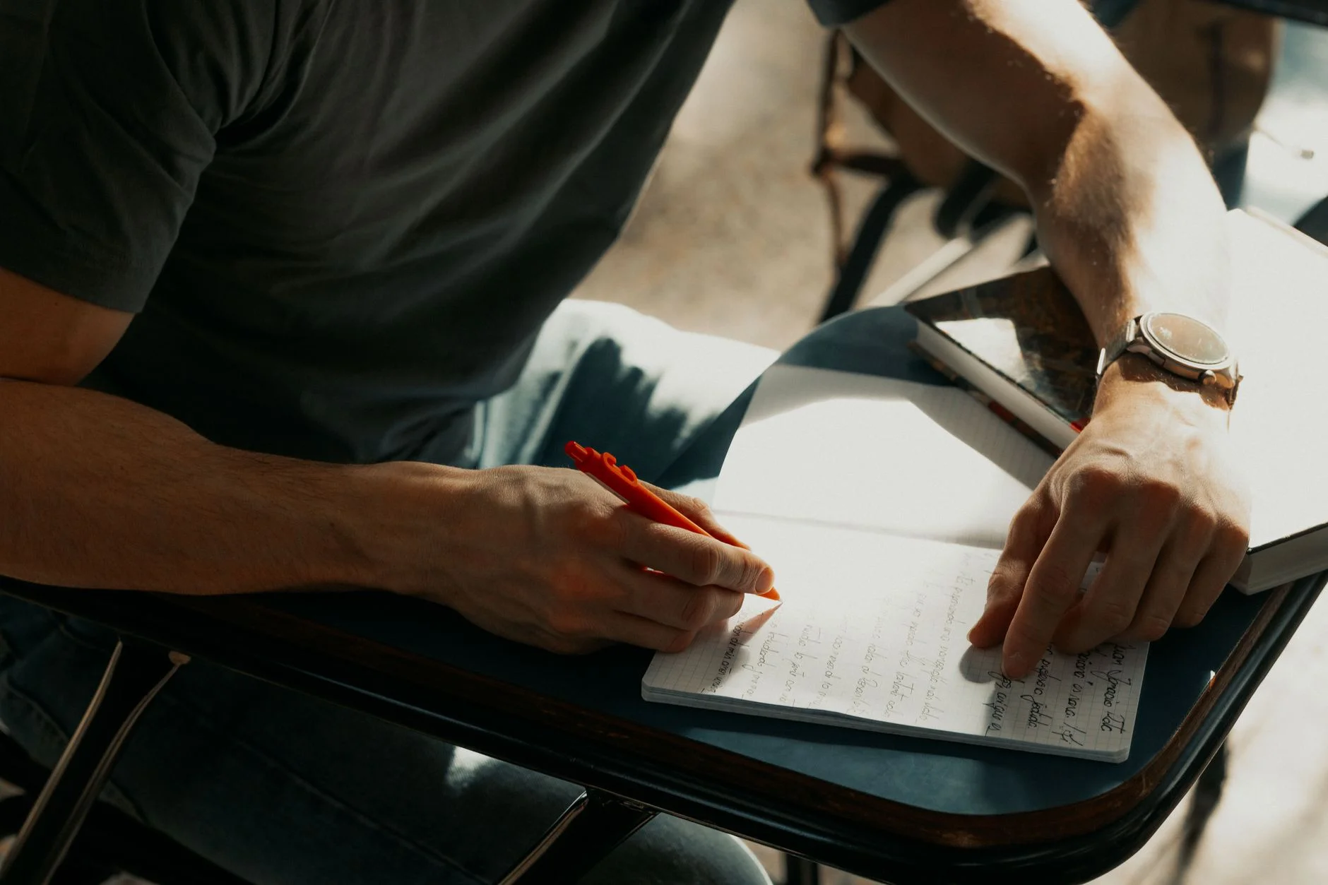 Close-up of a student writing notes with a red pen in a notebook on a classroom desk