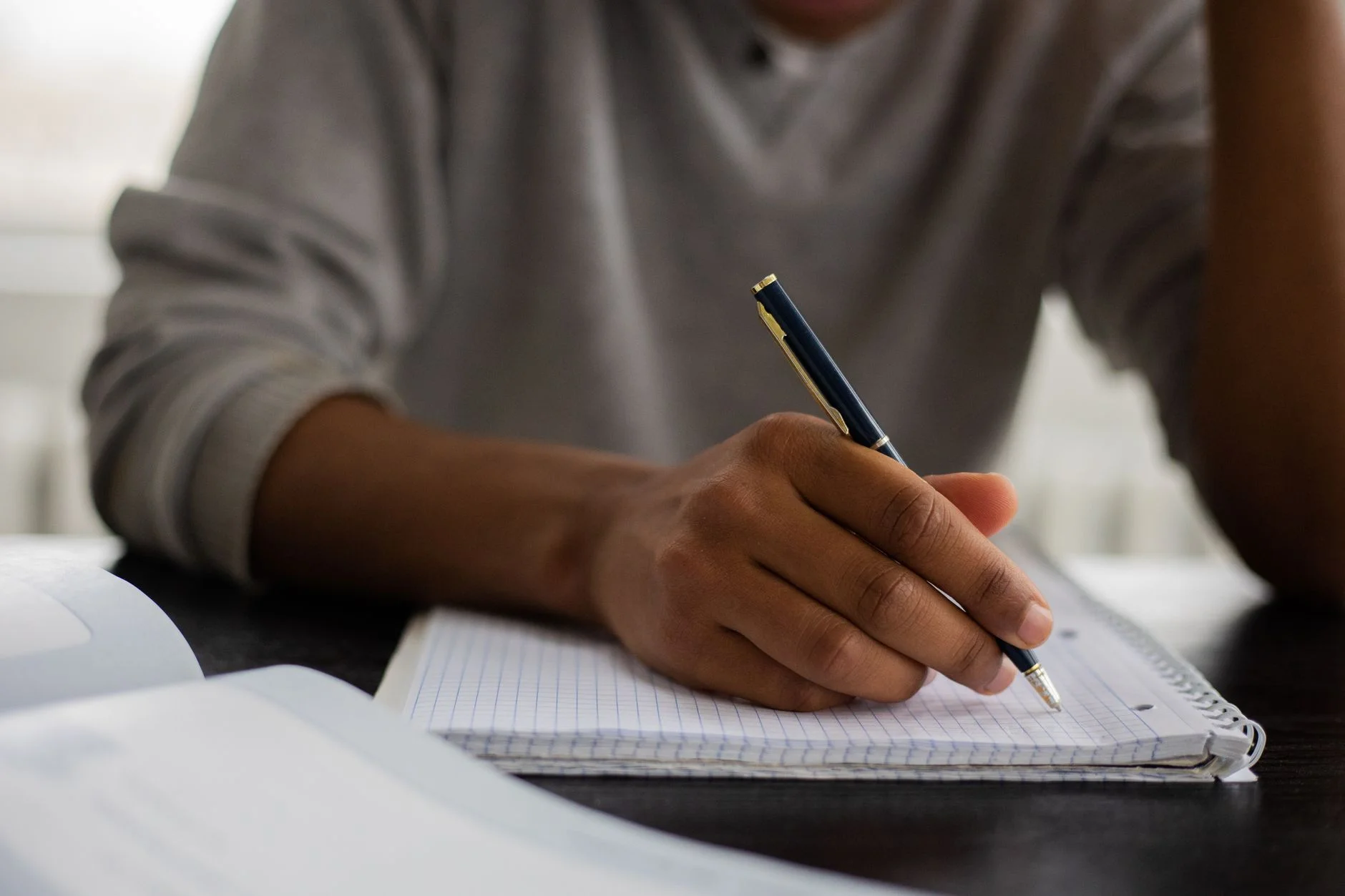 A student writing notes in a grid notebook next to an open book