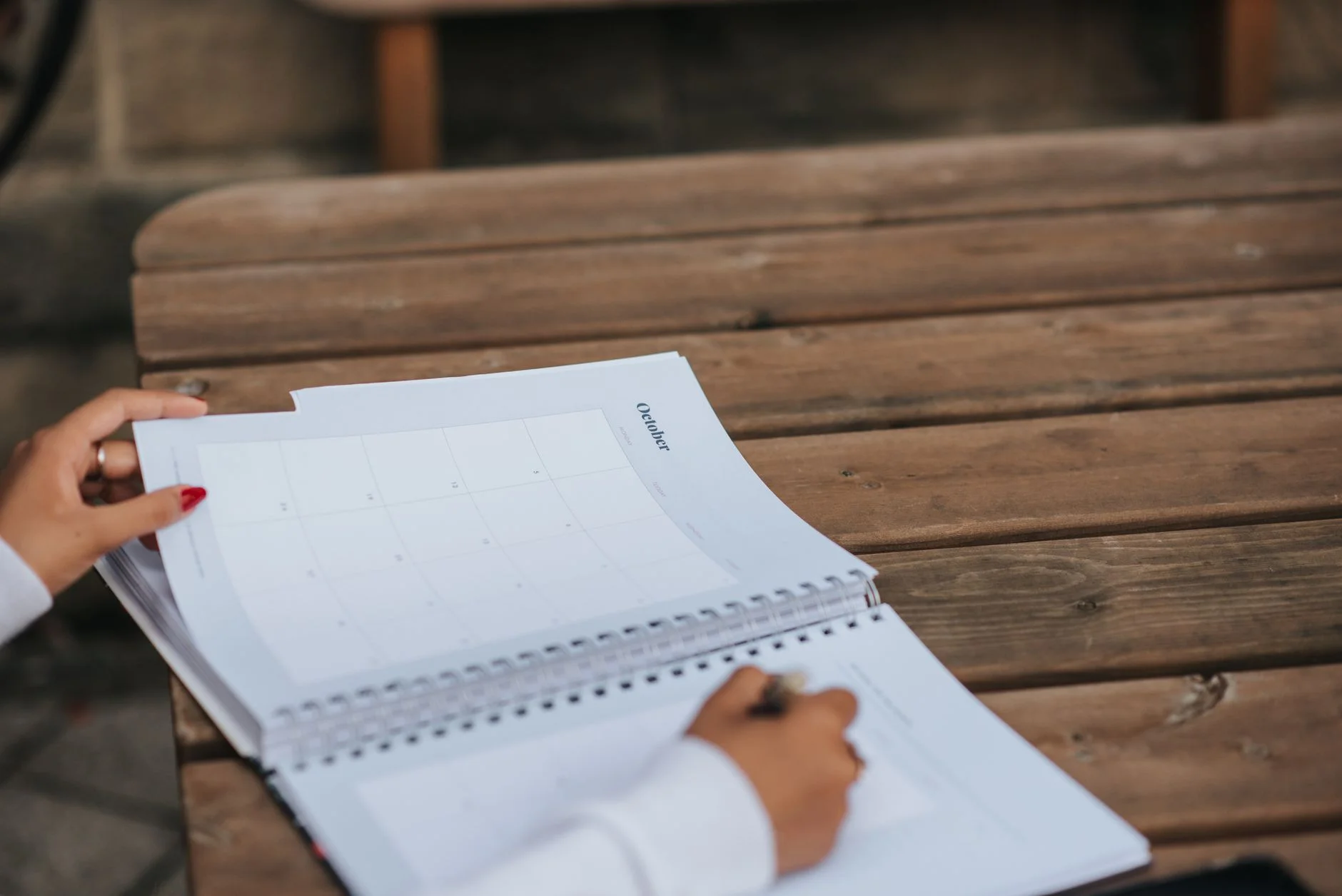 Person writing in an open monthly planner on a wooden outdoor table