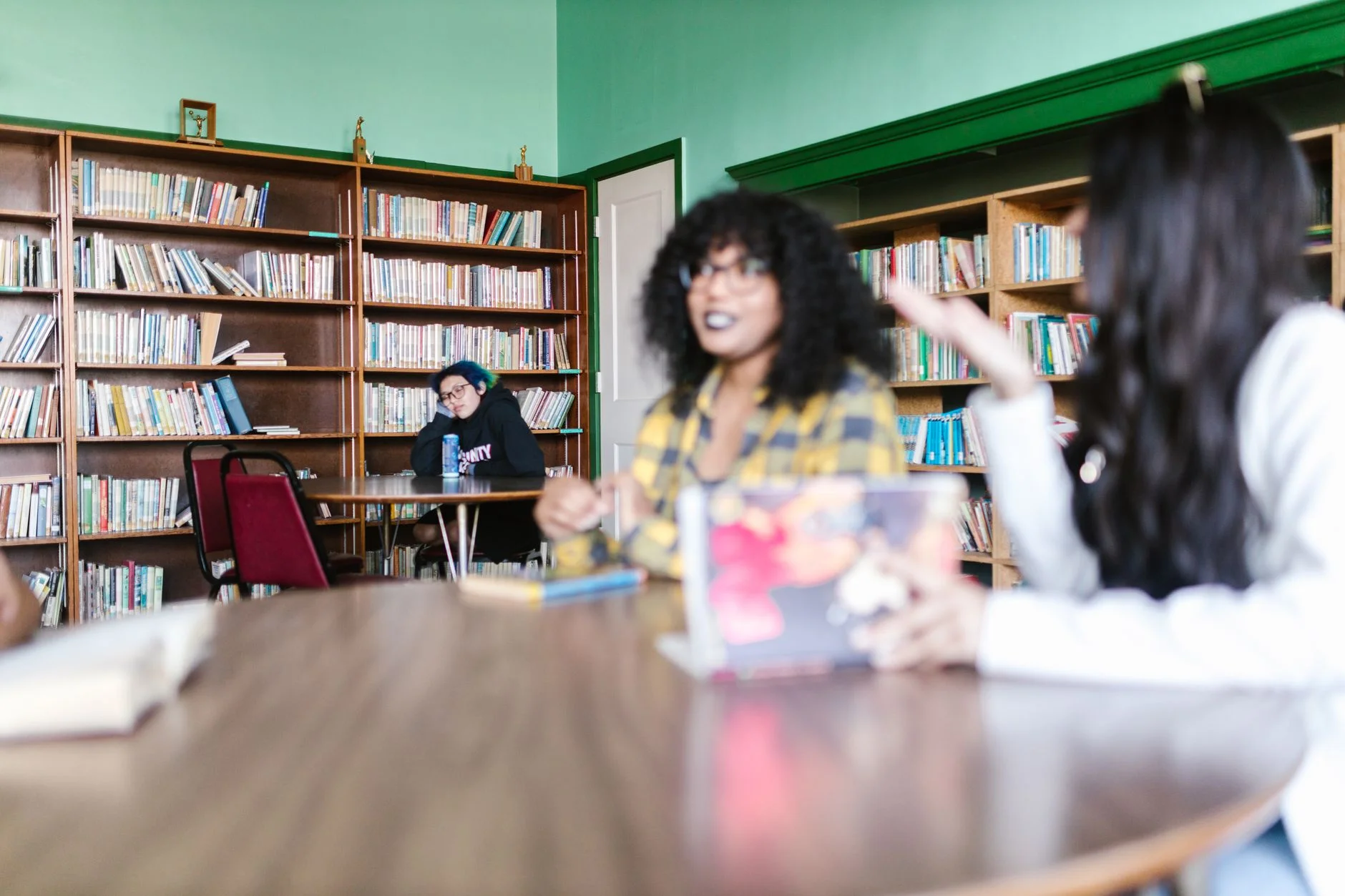 Students talking around a table in a library with shelves of books behind them
