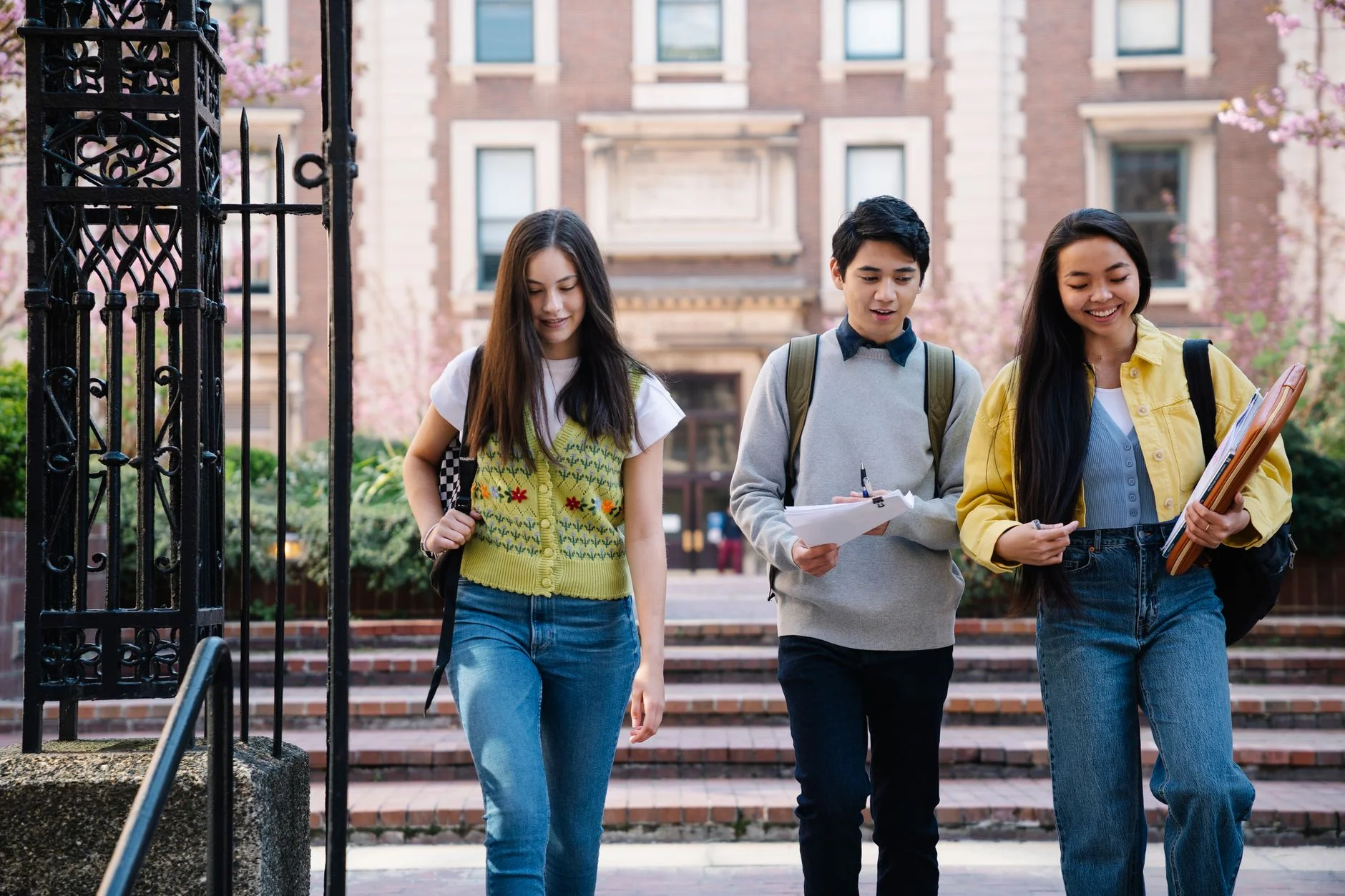 Three students walking together outdoors carrying notebooks and bags