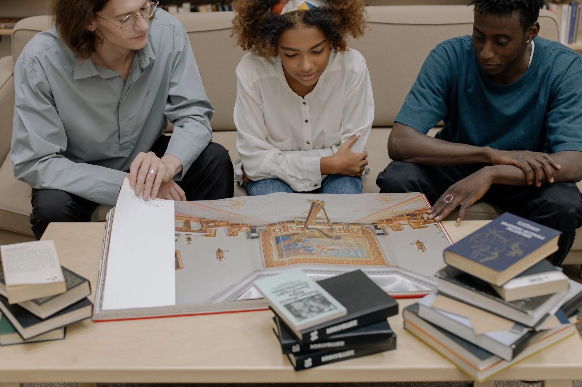 Three young people sitting together around a table covered with books and an open illustrated book