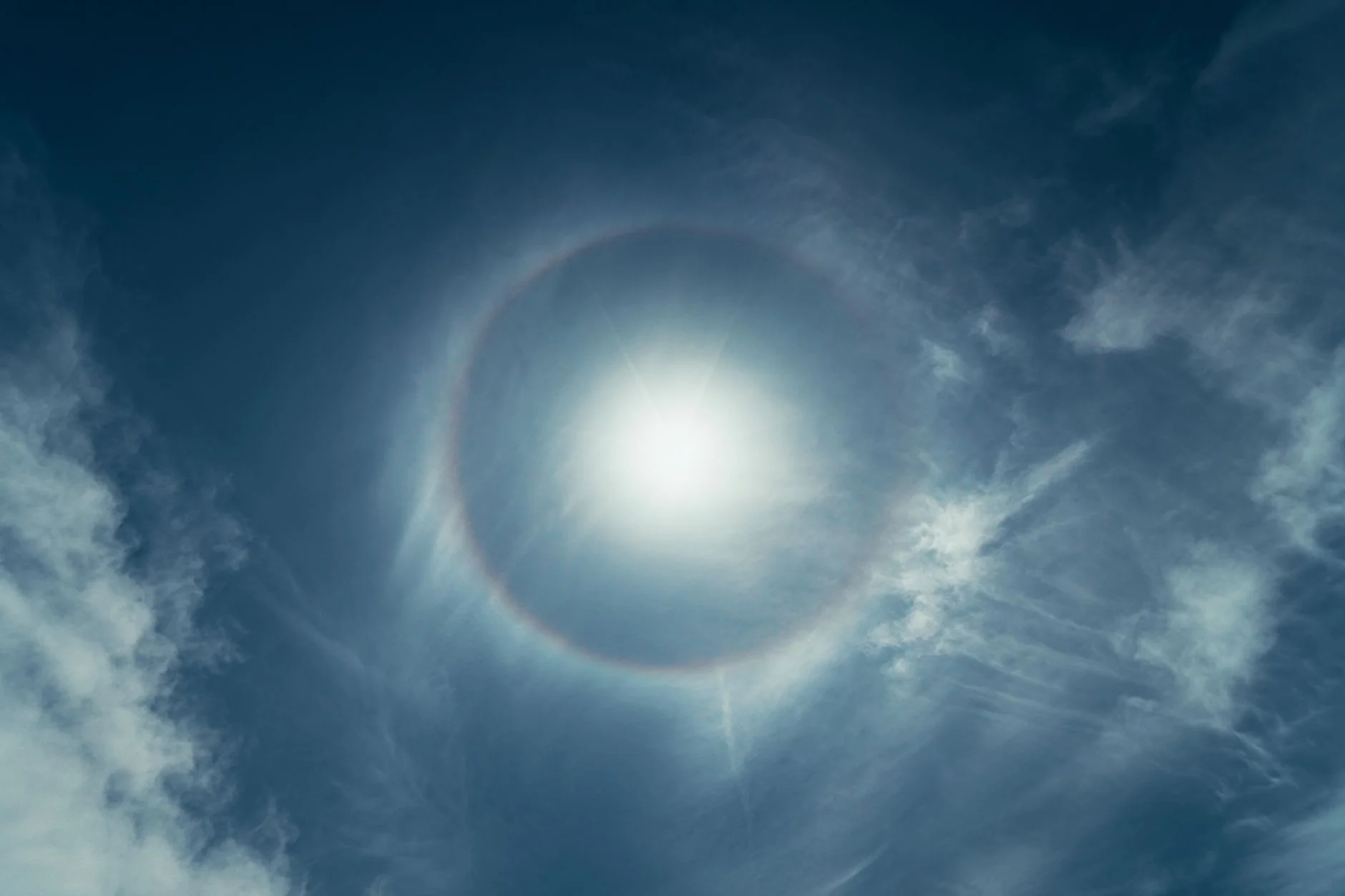 A 22 degree sun halo ring around the Sun in a blue sky with wispy cirrus cloud